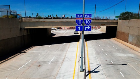 Empty highway lanes split under an overpass with signs directing I-10 East straight and I-10 West to the right.