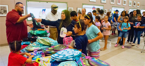 long line of kids waiting to receive backpacks piled on the table