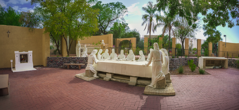A statue of Jesus stands prominently in the center of a serene courtyard surrounded by greenery.