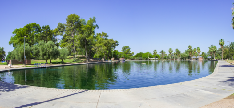 A large pond encircled by lush trees and vibrant bushes, reflecting the surrounding greenery.